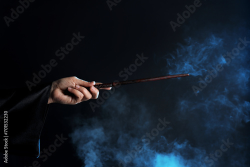 Magician holding wand in smoke on dark background, closeup