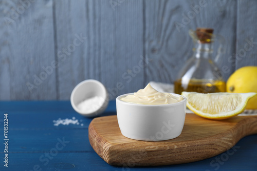 Tasty mayonnaise in bowl and lemon wedge on blue wooden table, space for text