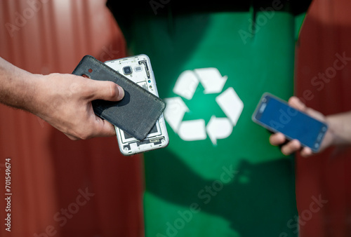 Man holding broken smartphone next to recycle bin, e waste concept 