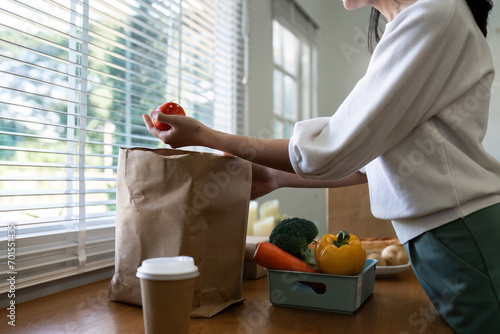 Organic Food Delivery. Happy young woman unpacking bag with Fresh Vegetables in kitchen photo