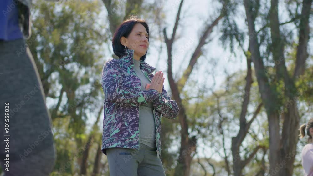Sportive middle aged woman holding hands in prayer position and practicing yoga during outdoor group class in the park. Medium long shot Sportive middle aged woman holding hands in prayer position and practicing yoga during outdoor group class in the park. Medium long shot
