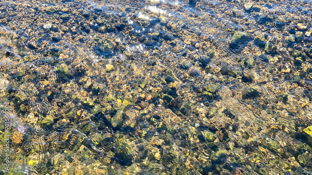 Real shot. A photograph taken from above the surface of a shallow, clear stream, revealing pebbles and sand with beautiful reflections. clear shallow
