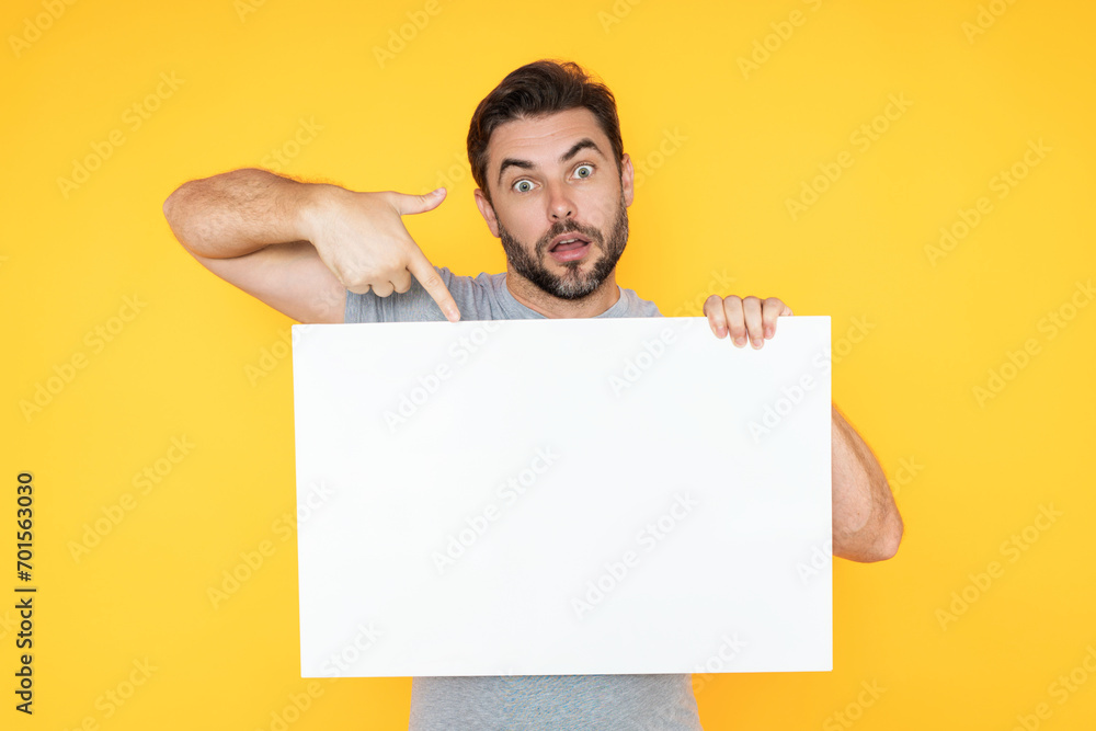 Guy with blank banner ad, isolated on studio background. Man holding empty blank poster showing placard pointing finger and gesturing index finger on board. Male presenting signboard or banner. Guy with blank banner ad, isolated on studio background. Man holding empty blank poster showing placard pointing finger and gesturing index finger on board. Male presenting signboard or banner.