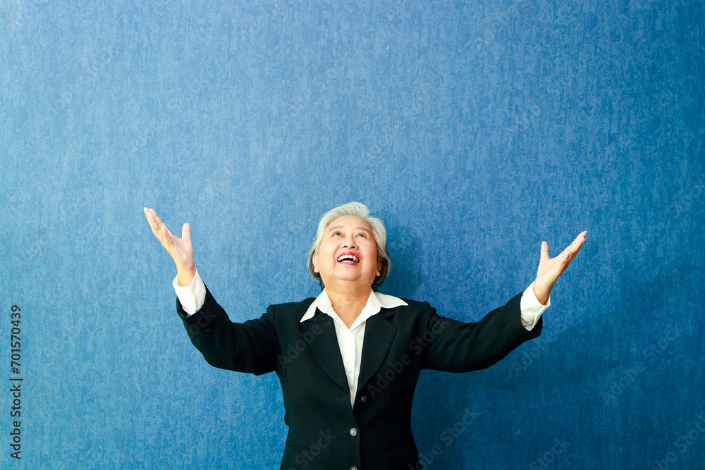 Elderly Asian business woman wearing a suit She smiles happily with both arms spread out on a blue background. business concept. copy space Elderly Asian business woman wearing a suit She smiles happily with both arms spread out on a blue background. business concept. copy space