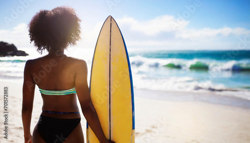 african american woman with surfboard looking at the ocean waves on the beach
