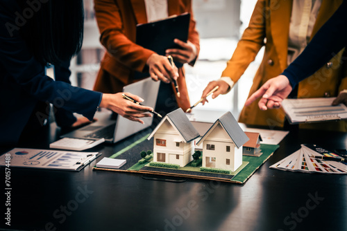 Asian real estate team engaged in a discussion, with two men and a woman focusing on a house model on a table, suggesting a planning or sales meeting.