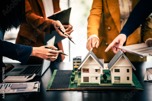 Asian real estate team engaged in a discussion, with two men and a woman focusing on a house model on a table, suggesting a planning or sales meeting.