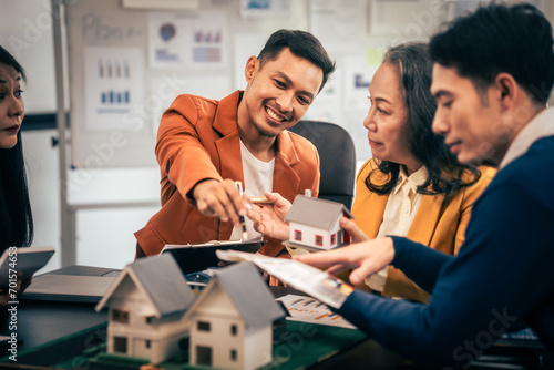 Asian real estate team engaged in a discussion, with two men and a woman focusing on a house model on a table, suggesting a planning or sales meeting.