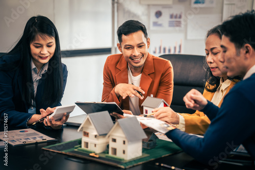 Asian real estate team engaged in a discussion, with two men and a woman focusing on a house model on a table, suggesting a planning or sales meeting. photo