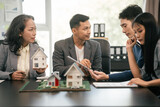 Asian real estate team engaged in a discussion, with two men and a woman focusing on a house model on a table, suggesting a planning or sales meeting.