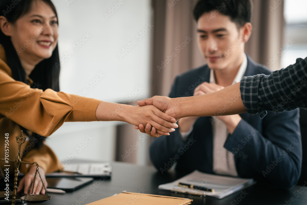 Asian woman yellow top shaking hands with someone across table, while Asian man in suit observes. Legal scales and books visible. legal, legislation Asian woman yellow top shaking hands with someone across table, while Asian man in suit observes. Legal scales and books visible. legal, legislation