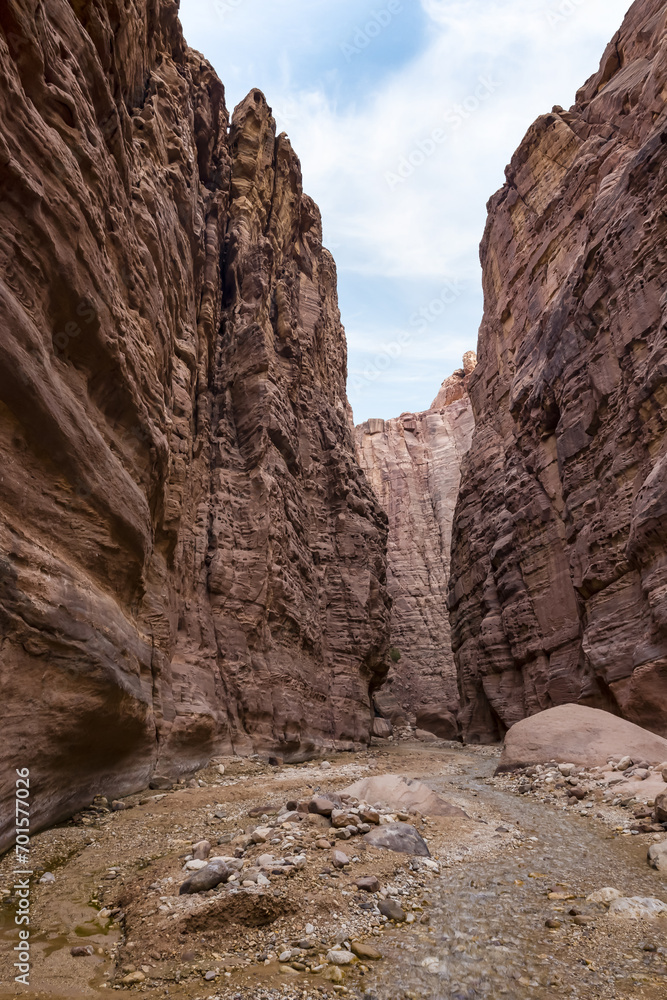 A shallow  stream flows between high mountains at beginning of the route along the Wadi Numeira hiking trail in Jordan