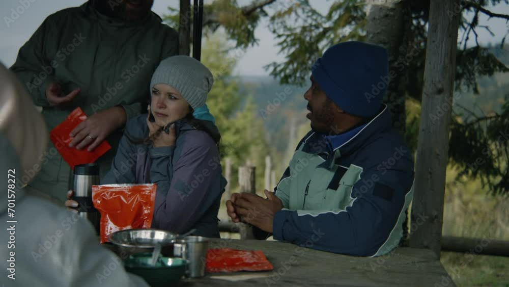 Adult African American man sits at the table in wooden gazebo and talks with friends. Group of diverse tourists resting in wooden gazebo during trek or hike in mountains in autumn. Tourism and travel. Adult African American man sits at the table in wooden gazebo and talks with friends. Group of diverse tourists resting in wooden gazebo during trek or hike in mountains in autumn. Tourism and travel.