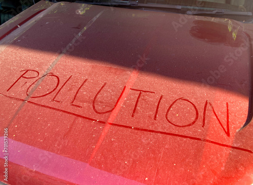 Hand writing the word POLLUTION on dust on a car hood