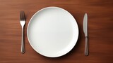 Empty white plate with knife and fork on wooden table.