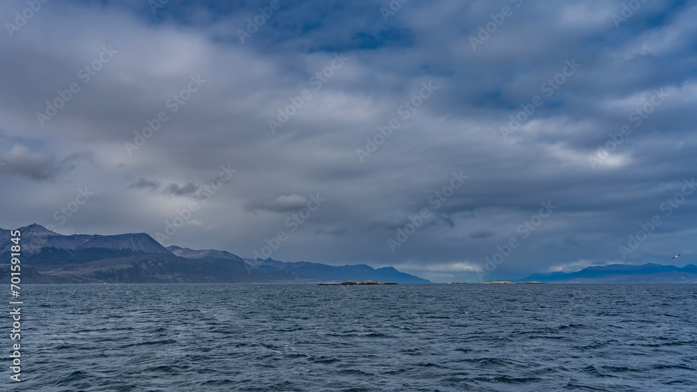 A calm seascape. Ripples on the surface of the blue ocean. Clouds in the azure sky. The Andes mountain range in the distance. Argentina. Beagle Channel. Tierra del Fuego Archipelago
