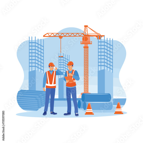 Structural engineers and architects wearing orange vests and safety helmets at a building construction site. Discuss the construction process over the phone and using a tablet at the building site.