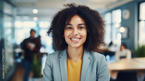 Portrait of young confidant business woman standing in the office smiling, co-workers and employees in the background photo