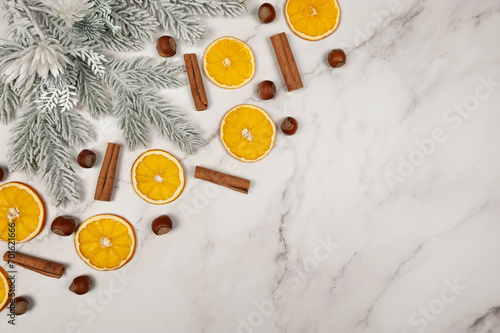 Christmas composition, dried orange slices, fir tree branches, cinnamon sticks, hazelnuts on white marble background. Christmas, New Year, winter concept. Top view, flat lay, copy space.