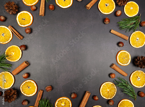 Christmas composition, dried orange slices, fir tree branches, cinnamon sticks, pine cones, hazelnuts on black stone background. Christmas, New Year, winter concept. Top view, flat lay, copy space.