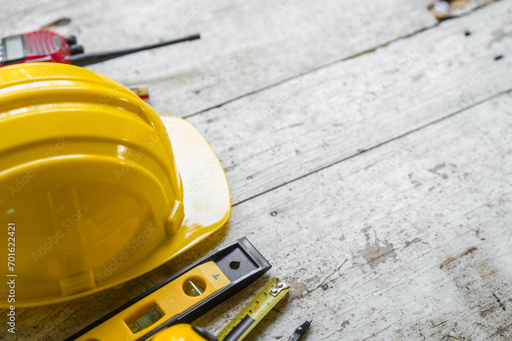 Fototapeta premium Top view construction tools such as a yellow hard hat, spirit level, measuring tape, folding ruler arrayed against a wooden plank background.