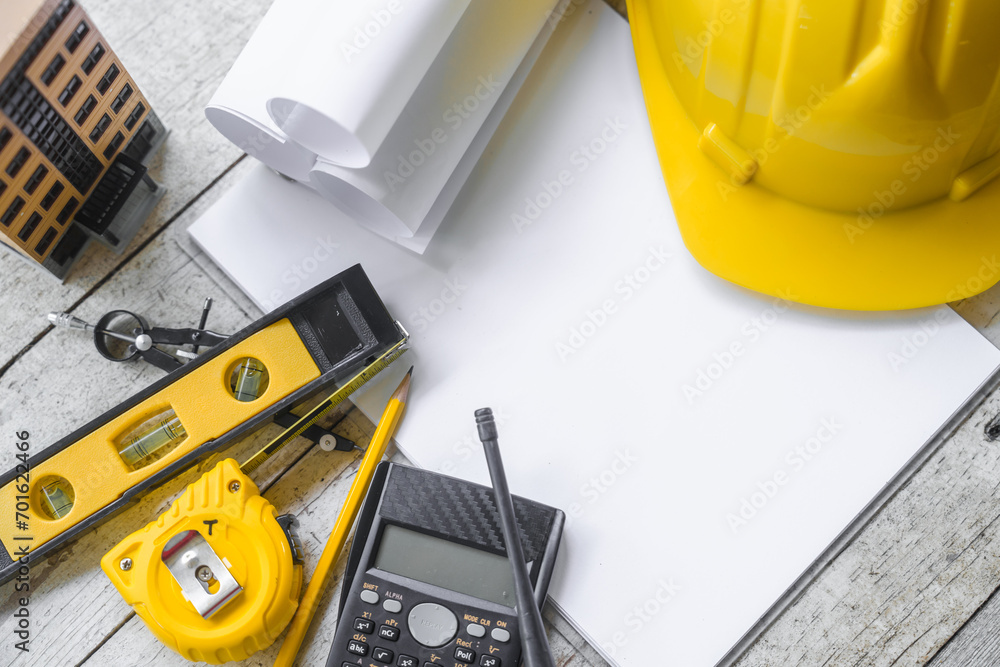 Top view construction tools such as a yellow hard hat, spirit level, measuring tape, folding ruler arrayed against a wooden plank background. Top view construction tools such as a yellow hard hat, spirit level, measuring tape, folding ruler arrayed against a wooden plank background.