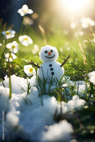 Snowman on a meadow with grass and spring flowers growing through the melting snow. Concept of spring coming and winter leaving.