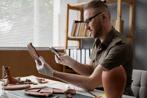Archaeologist using magnifying glass working in office to study artifacts