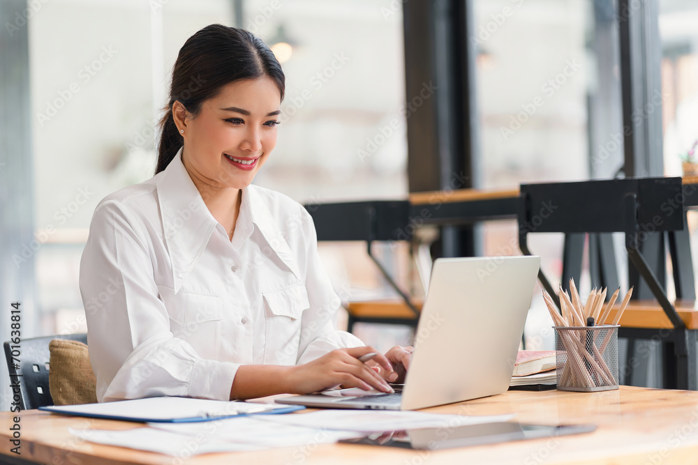 Beautiful asian businesswoman smiling while working with laptop computer at a Modern Co working Space. Remote work concept Beautiful asian businesswoman smiling while working with laptop computer at a Modern Co working Space. Remote work concept