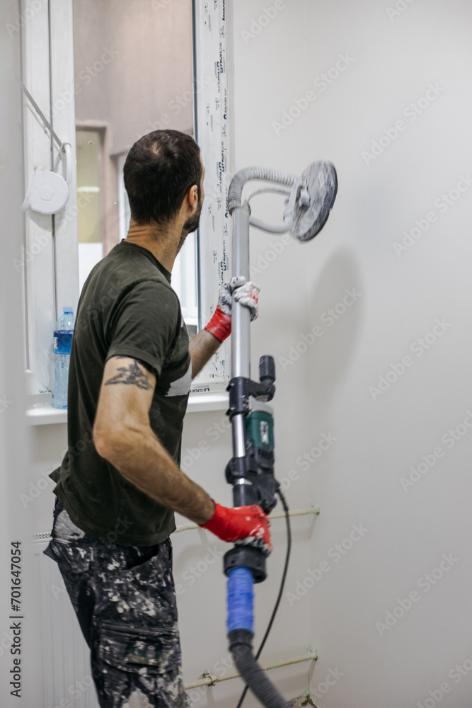 Man working on big apartment renovation project and using a wall smoothing machine. Man working on big apartment renovation project and using a wall smoothing machine.