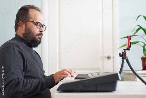 Man playing electric piano and vlogging with smart phone at home photo