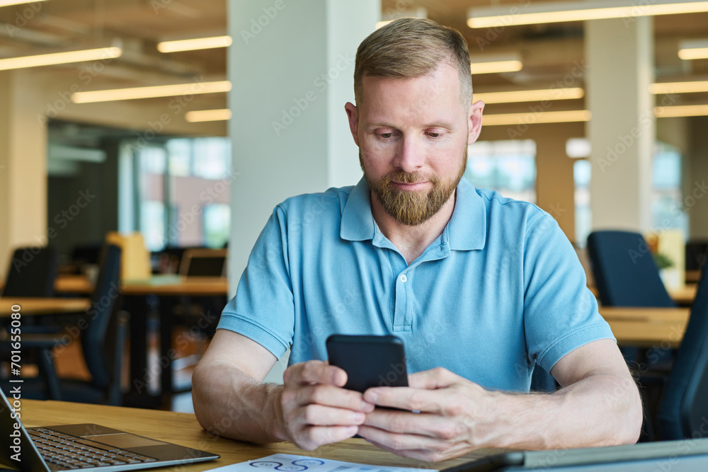 Businessman using smart phone near laptop at desk in office Businessman using smart phone near laptop at desk in office