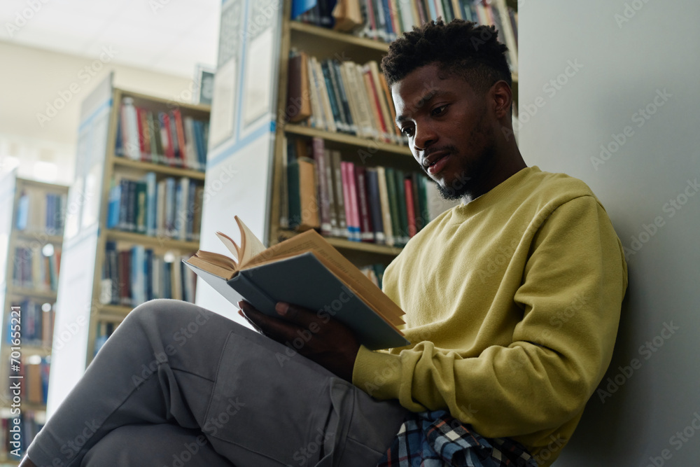 Student leaning on shelf and reading book in library Student leaning on shelf and reading book in library