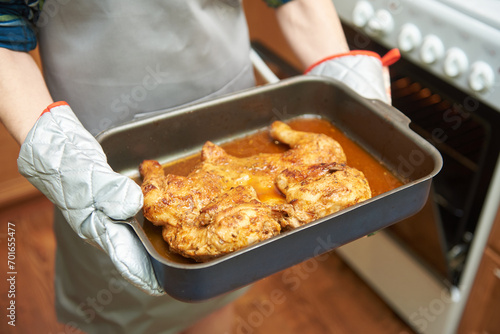 The female hands holds a cooked chicken from the oven