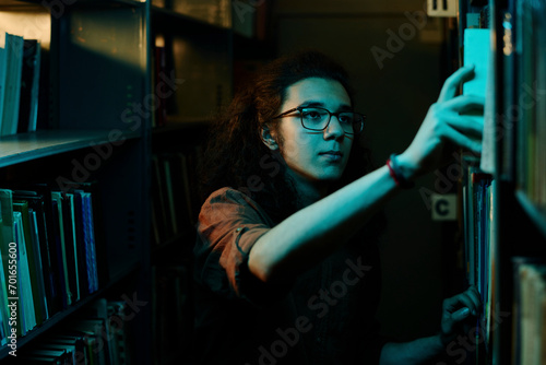 Student choosing book from shelf in library photo