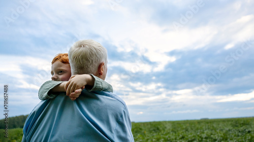 Grandfather carrying grandson in field under cloudy sky at sunset photo