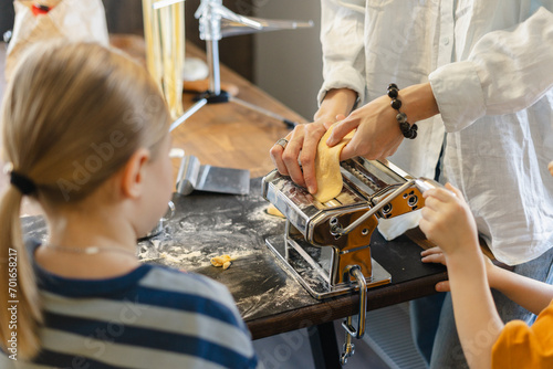 Woman cutting dough in pasta maker with son and daughter at home photo