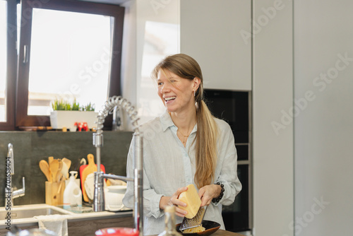 Happy woman grating cheese in kitchen at home photo