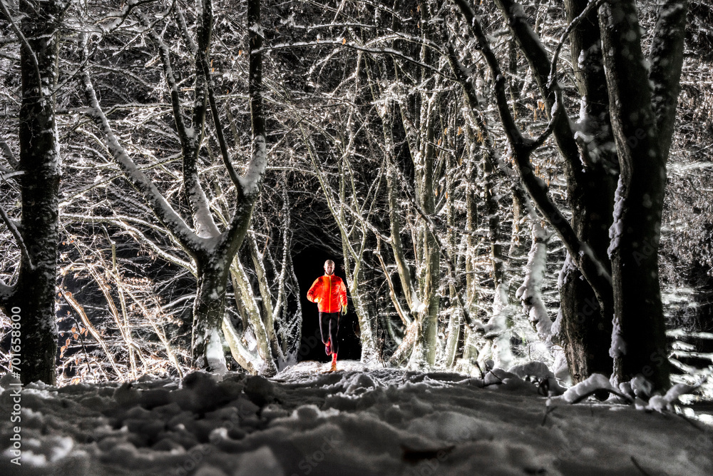 Man running on snow under trees in winter forest at night Man running on snow under trees in winter forest at night