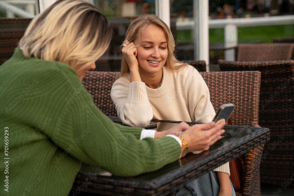 Happy woman with friend using smart phone at table in cafe Happy woman with friend using smart phone at table in cafe