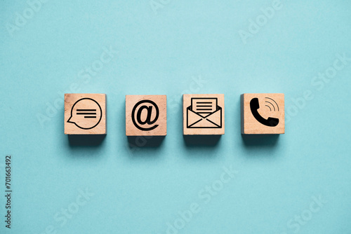 Contact icons include message address e-mail and telephone on wooden block cube and blue background for customer hotline service support concept. photo