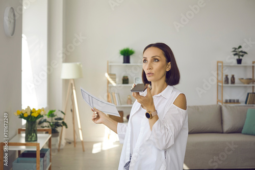 Busy woman recording voice message. Serious lady talking on speaker mode. Business executive manager holding phone, using messenger app, sending employee audio text, giving order, making arrangement photo
