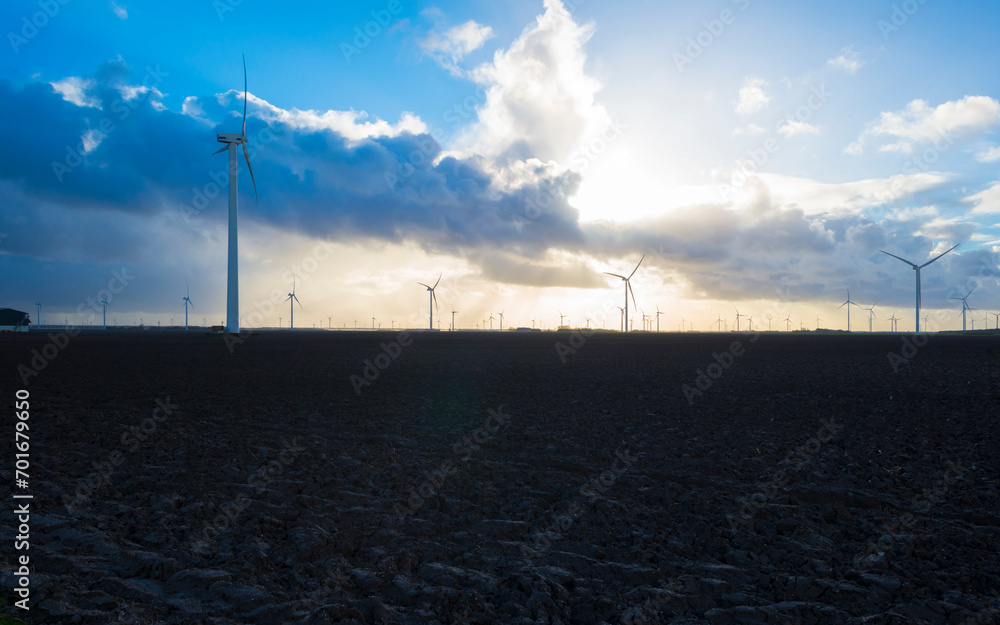 Wind turbines on the horizon of an agricultural field along a ditch in bright sunlight in winter, Almere, Flevoland,  Netherlands, January 1, 2024