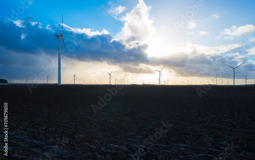 Wind turbines on the horizon of an agricultural field along a ditch in bright sunlight in winter, Almere, Flevoland, Netherlands, January 1, 2024