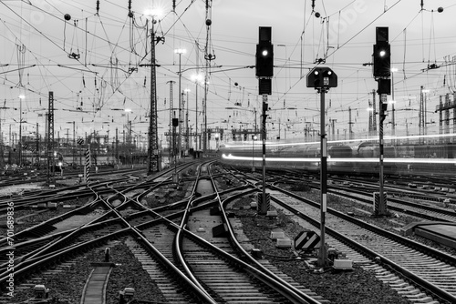 Railway infrastructure at Frankfurt main station, Germany. Black and white panorama. Technology with signals, crossings, catenary, tracks, switches at twilight. Blurred fast train lights in motion.  photo