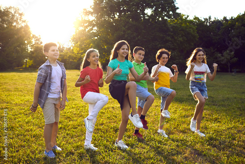 Excited boys and girls playing active games outdoors. Happy children standing, balancing on one leg and doing thumbs up gesture with both hands in park. Outdoor leisure activities concept