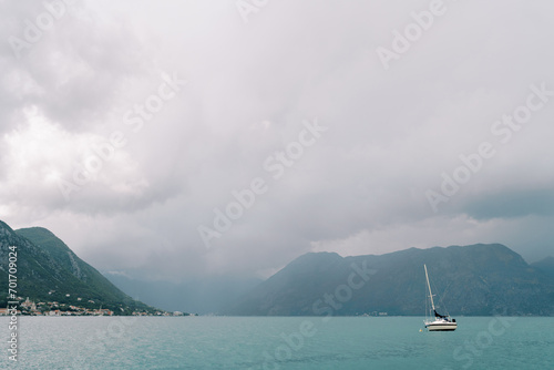 Sailing yacht sails on the sea against the backdrop of mountains in the fog