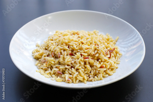 Cooked brown rice in white plate on dark background.