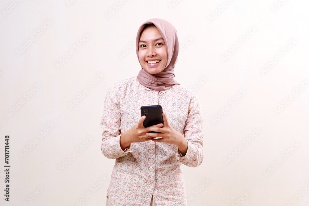 Happy smiling young asian muslim woman holding a cell phone while looking at the camera. Isolated on white background Happy smiling young asian muslim woman holding a cell phone while looking at the camera. Isolated on white background