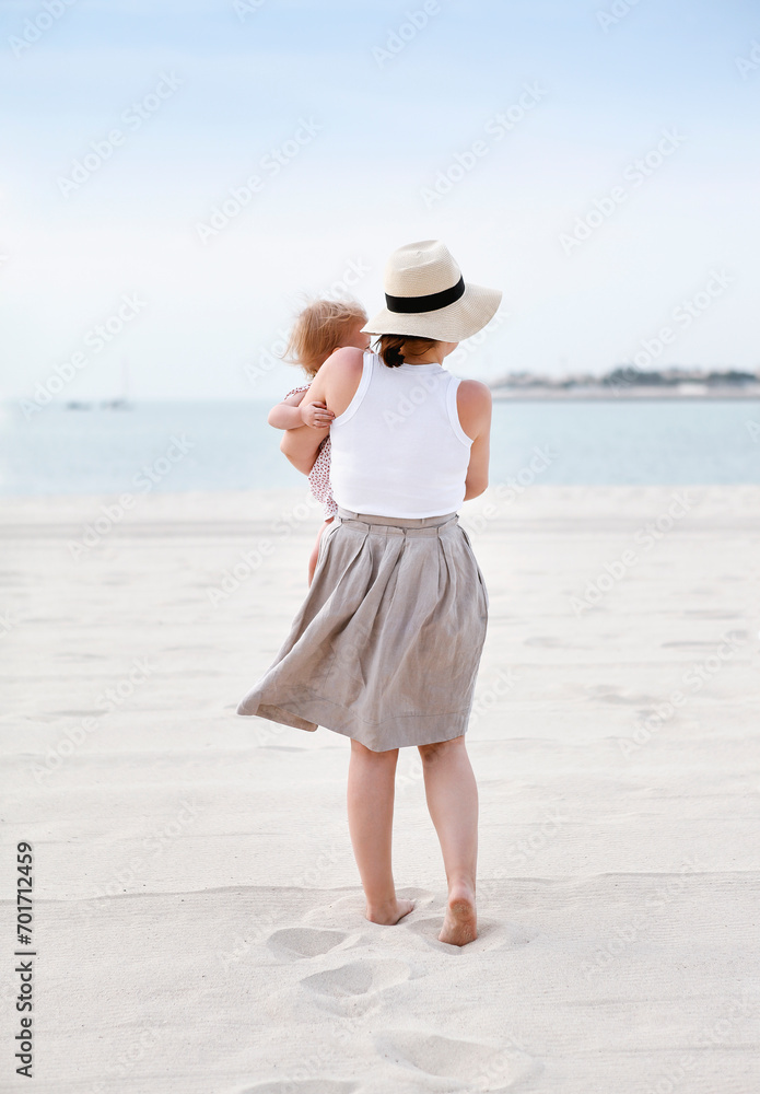 Woman with baby standing on sandy beach